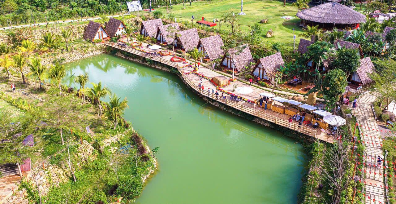 A riverside resort with thatched-roof huts, a wooden walkway, and a calm river.
