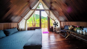 A cozy attic room with a bed, a table with items, and a view of greenery outside. - LEAF VILLAGE & FARM LÀNG LÁ (Da Nang)