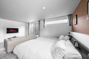 Ein modernes Hotelzimmer mit einem großen Bett, einer Couch, einem an der Wand befestigten Fernseher und einem Fenster mit Vorhängen.