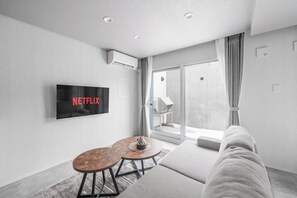 Ein modernes Wohnzimmer mit Flachbildfernseher, einer Couch, einem Couchtisch und einer Glastür, die auf einen Balkon führt.
