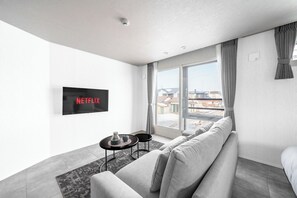 A modern hotel room with a large window, a sofa, a small table, and a wall-mounted TV displaying 'NETFLIX'. - GRAN HILLS 202 / Chitose City Hokkaidō (Chitose City)
