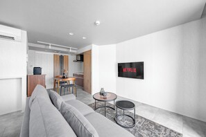 A modern living room with a grey sofa, a small round table, and a TV mounted on the wall. - GRAN HILLS 202 / Chitose City Hokkaidō (Chitose City)