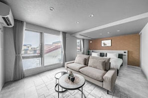 Moderni hotellihuone, jossa on suuri ikkuna, sohva, pieni pyöreä pöytä ja sängyssä pääty.