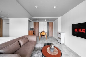 Quarto de hotel moderno com sofá, mesa de jantar, televisão e minibar.