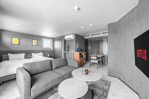 Une chambre d’hôtel moderne équipée d’un lit, d’un canapé, de deux petites tables rondes, d’un bureau et d’un téléviseur fixé au mur.
