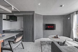 Une cuisine moderne dotée d’un four encastré, un coin repas avec une table et des chaises, et un espace de vie avec un téléviseur fixé au mur.