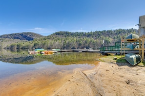Blick auf einen See mit Booten, einer Anlegestelle und einem bewaldeten Hügel.