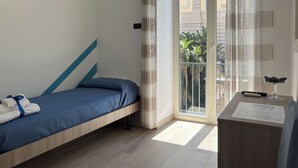 Una habitación con cama, una mesita con un control remoto y vistas a un balcón con plantas.