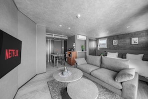 A modern living room with a grey sofa, a coffee table, a TV mounted on the wall, and a dining area in the background. - GRAN HILLS 401 / Chitose City Hokkaidō (Chitose City)