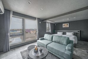Une chambre d’hôtel moderne dotée d’une grande fenêtre, d’un canapé, d’un lit et d’une petite table agrémentée d’objets décoratifs.