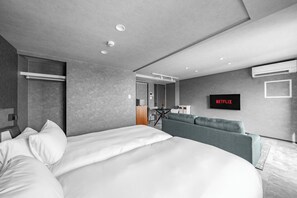 Une chambre d’hôtel moderne avec un grand lit, un canapé gris, un téléviseur à écran plat et un espace bureau.