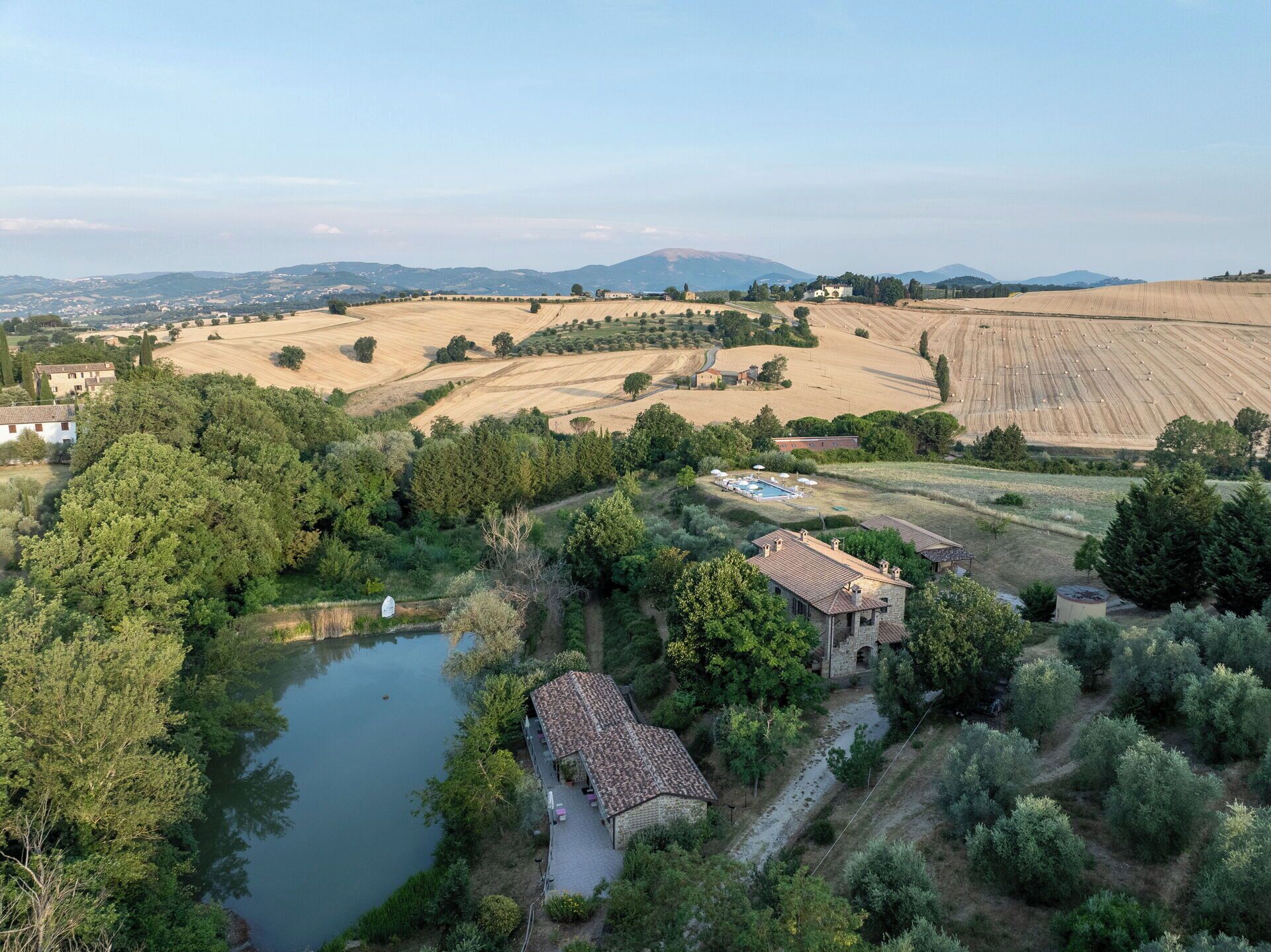 A rural landscape with a pond, a stone building with a tiled roof, and expansive fields.
