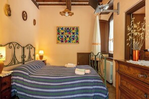Une chambre à coucher avec un lit, une commode en bois, un tableau, une lampe et une fenêtre avec des rideaux.