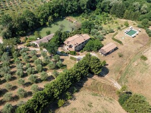 Vue aérienne d’une propriété rurale comprenant un grand bâtiment, une piscine et une végétation luxuriante.