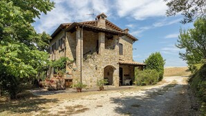 Un edificio in pietra con un portico coperto, un vialetto sterrato e vegetazione circostante.