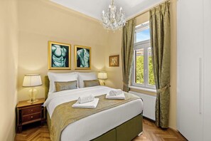 Une chambre à coucher bien aménagée, avec un lit, deux tables de chevet, un lustre et des œuvres d’art accrochées au mur.