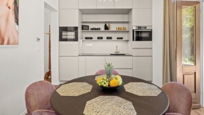 A modern kitchen with white cabinets, a chandelier, and a dining table with placemats and fruit. - App Nia - Villa Accione (Opatija)