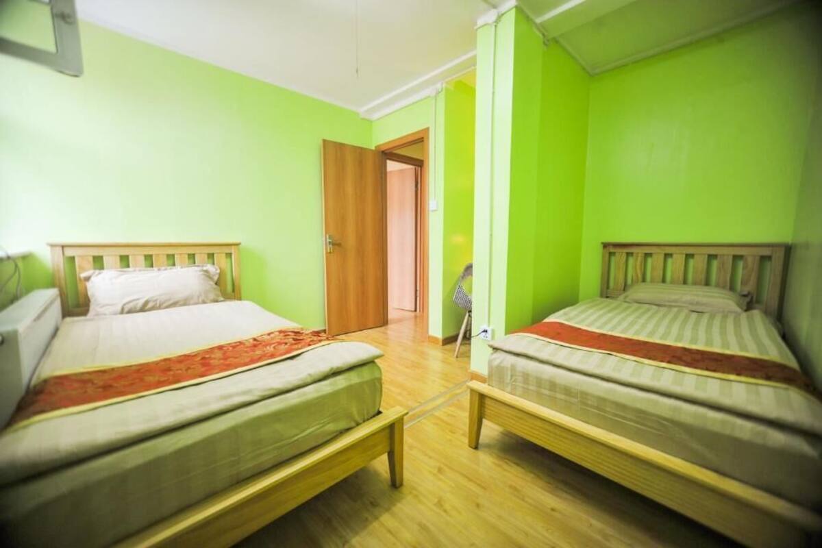 A room with two single beds, wooden headboards, a wooden floor, and a door leading to another room.
