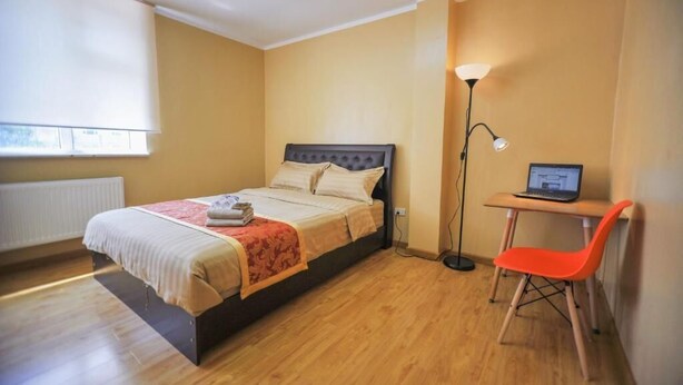 A bedroom with a bed, a desk with a laptop, a chair, and a floor lamp. - Mongolian Vision Tours (Ulaanbaatar)