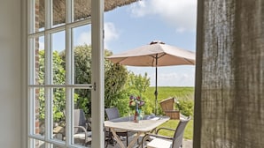 An open door to a patio with a table, chairs, a table umbrella, and a vase with flowers.