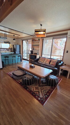 Uma sala de estar ampla com piso de madeira, um sofá com almofadas estampadas, uma mesa de centro e uma televisão.