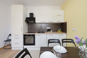 A compact kitchen with white cabinets, a black stove, and a dining area with a table set for two. - Cozy Apartment | Place to Work | Pet Friendly (Warszawa)