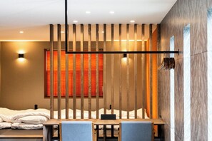 Et moderne hotelværelse med en seng, et bord med stole, en rumdeler med lodrette lister og en vægmonteret lampe.