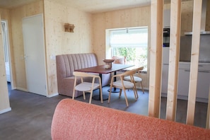 A room with a wooden wall, a sofa, a dining table with chairs, a window, and a kitchenette.