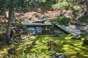 Een rustige tuin met een klein vijvertje, een zitgedeelte van natuursteen en weelderige begroeiing.