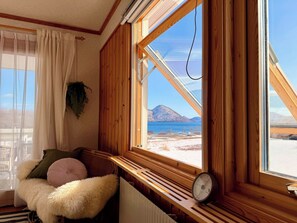 Habitación acogedora con un banco de madera, un radiador y un ventanal con vistas a una playa y montañas.