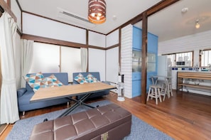 Una sala de estar moderna con un sofá, una mesa de centro, un banco y una zona de cocina con microondas y taburetes de bar.