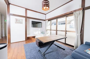 Una habitación con una mesa de madera, un sofá azul, un televisor y un ventanal con cortinas.