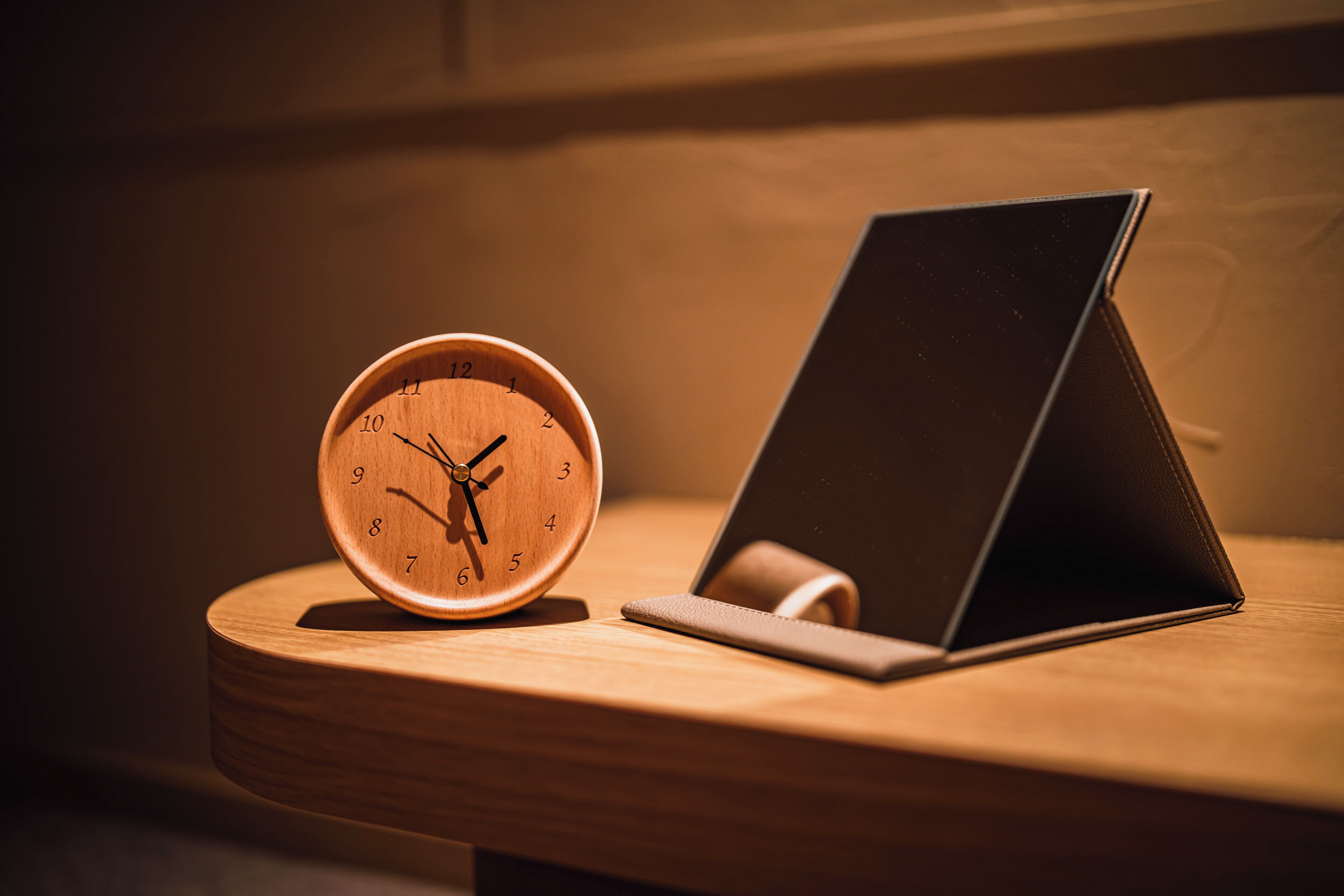 A wooden table with a wooden clock and a black laptop on it.