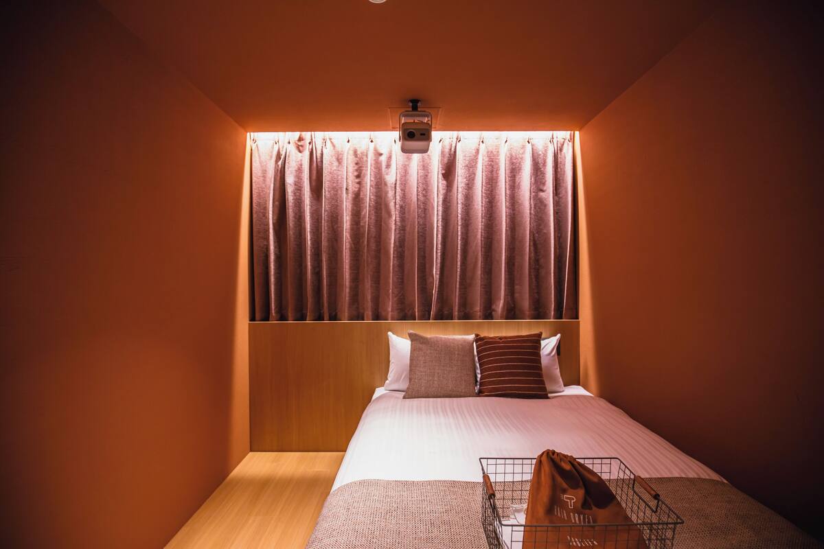 Habitación de hotel con cama, cabecero, mesita de noche y lámpara de pared.
