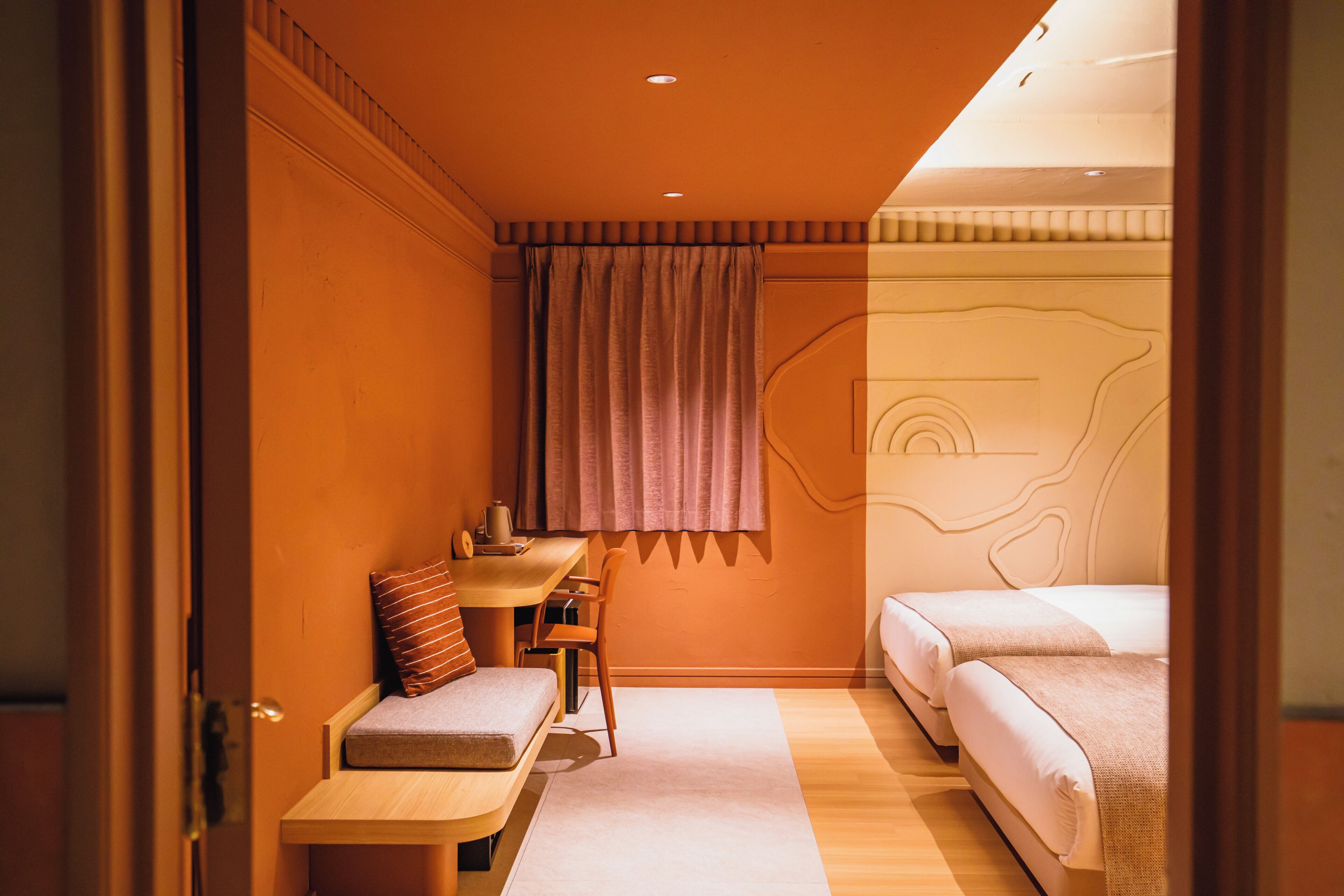 A compact hotel room with a bed, a small desk, a chair, and a window with curtains.