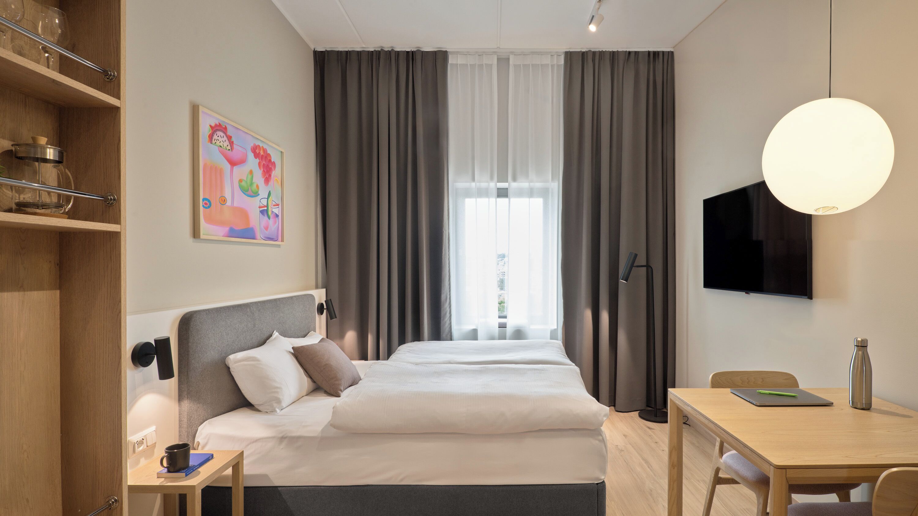 A hotel room with a bed, bedside table, desk, chair, TV, and a window with curtains.