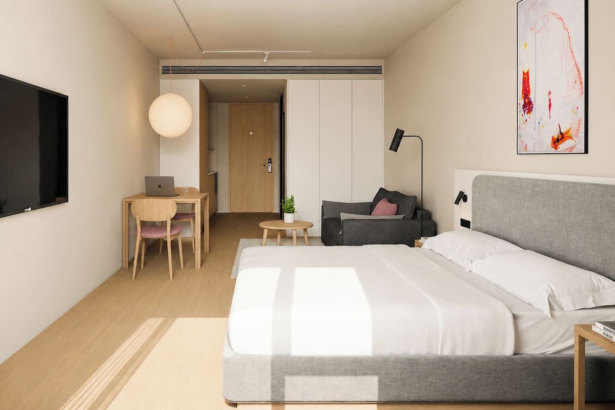 Ein modernes Hotelzimmer mit Bett, Schreibtisch, Stuhl und einem Fernseher an der Wand.