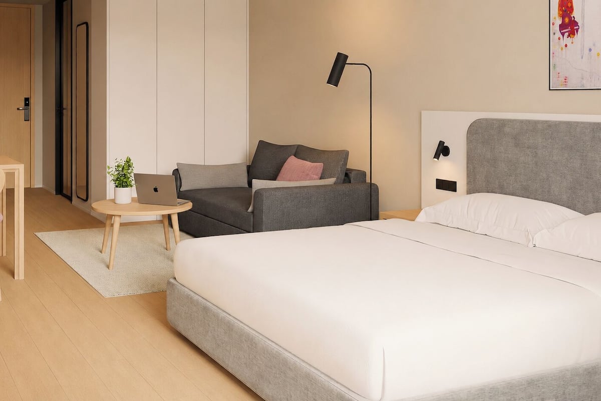 Ein modernes Hotelzimmer mit einem Bett, einem Schreibtisch, einem Stuhl, einer Couch, einem kleinen Tisch mit einer Pflanze und einer Lampe.