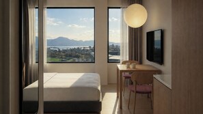 A hotel room with a bed, a desk, a chair, a TV, and a view of mountains and a city. - Stey Stavanger (Stavanger)