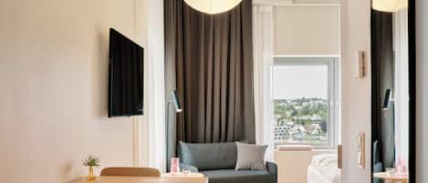 A modern hotel room with a dining table, sofa, and a view of a cityscape.