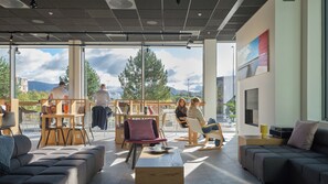 Ein moderner Innenraum mit Sitzgelegenheiten, Bücherregalen und großen Fenstern mit Blick ins Freie.