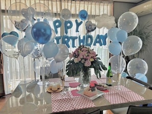 Une pièce avec une table en verre, des ballons, un gâteau et une pancarte où l’on peut lire « Joyeux anniversaire ».