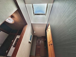 Um corredor estreito com um claraboia, portas de madeira e uma abertura de ventilação.