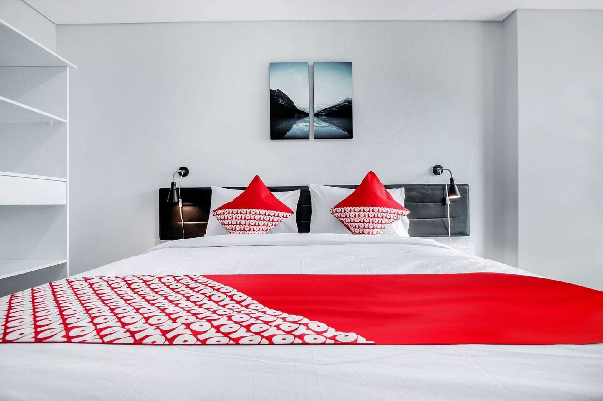 A modern bedroom with a bed, red and white pillows, a black headboard, and a wall-mounted artwork.