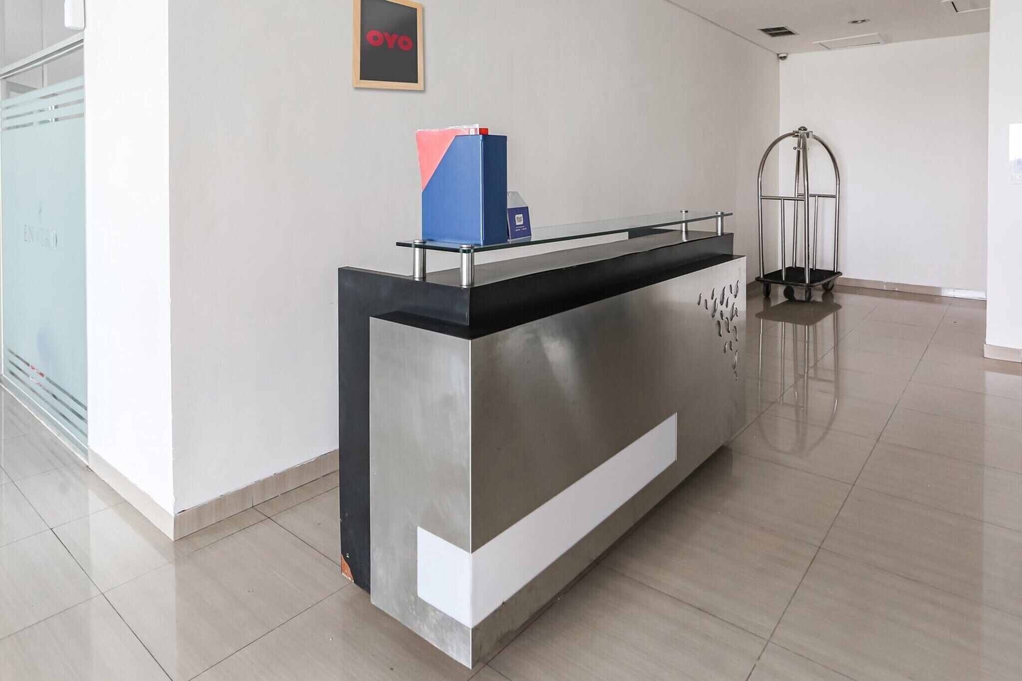 A reception desk with a glass top, a blue and pink folder on it, and a metal cart in the background.