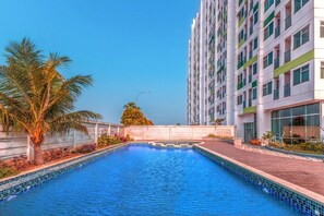 A swimming pool with a tiled edge, a palm tree, and a multi-story building with balconies. - Cozy Double Escape W/ Free WiFi and Parking (Bekasi)