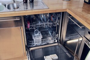 A stainless steel dishwasher in a kitchen with a wooden countertop and a sink.