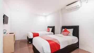 A hotel room with two beds, a TV, a desk, and an air conditioning unit.