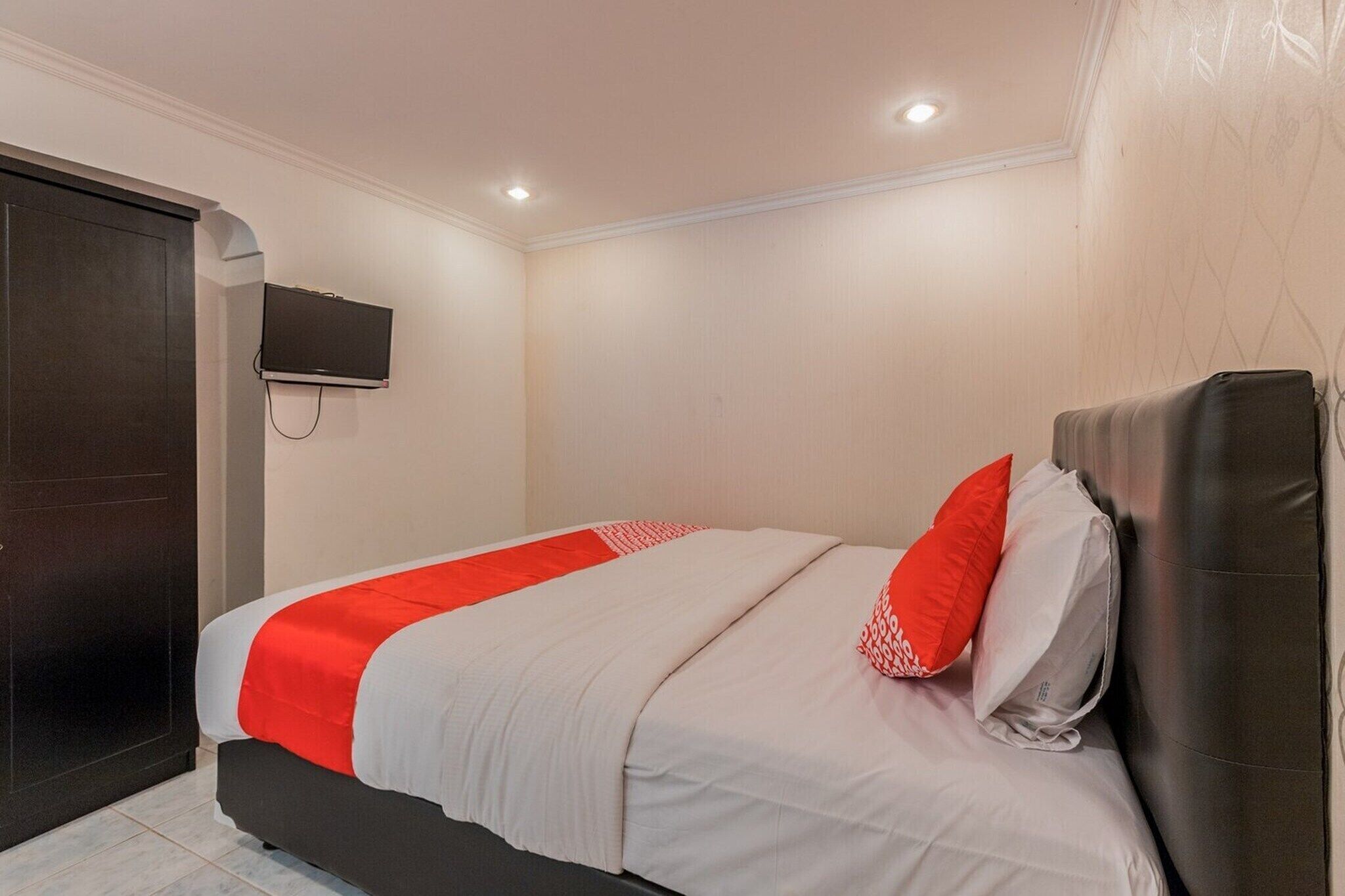 A hotel room with a bed, a TV mounted on the wall, and a door.