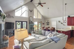 Un salón amplio con chimenea, ventilador de techo y comedor con vistas.